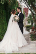 © sonyachny - Gorgeous bride and stylish groom gently hugging on background of green trees. Sensual wedding couple embracing. Romantic moments of newlyweds. Modern wedding photo