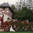 © sonyachny - Gorgeous bride and stylish groom gently hugging and smiling at  old wall of autumn red leaves. Happy sensual wedding couple embracing. Romantic moments of newlyweds