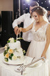 © sonyachny - Gorgeous bride and stylish groom cutting together white wedding cake with roses at wedding reception. Happy wedding couple tasting cake. Romantic moments of newlyweds