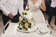 © sonyachny - Gorgeous bride and stylish groom cutting together white wedding cake with roses at wedding reception. Happy wedding couple tasting cake. Romantic moments of newlyweds