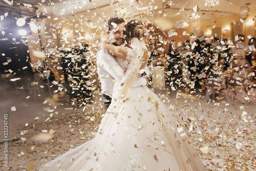 Fotomural Gorgeous bride and stylish groom dancing under golden confetti at wedding reception