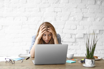 Frustrated young woman looking at laptop with stressed facial expression, keeping hands on head, troubled with shocking news. Unexpected computer crash, shocking news, fatal error, data loss