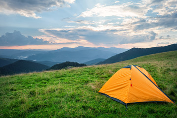 Wall Mural - orange tent on green grass in mountains in summer