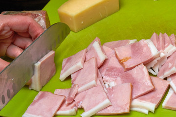 Hand holds ham and slices meat on a cutting board