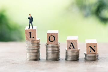 Miniature people businessmen standing with wood word LOAN stack of coins to thinking and planning. using as background Money, Financial, Business Growth concept with copy space.