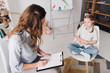 © LIGHTFIELD STUDIOS - high angle view of psychologist with clipboard talking to little child in office