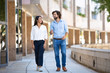 © KAMPUS - Smiling multiethnic business partners talking at walking in city. Professional latin and hispanic colleagues on break near office building. Businesspeople concept