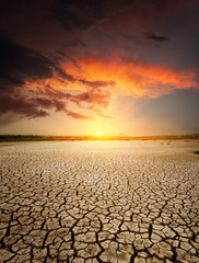 Wall Mural - red sunset in dramatic clouds over drought earth