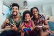 © Mediteraneo - Smiling family sitting on the couch together playing video games