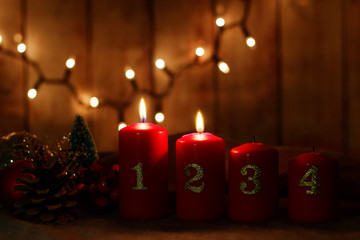 Four Advent candles (two lighted) with numbers and Christmas decoration. Lights in the background on wooden wall