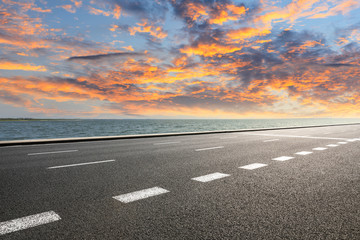 Asphalt road and dramatic sky with coastline at sunset