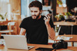 © VadimGuzhva - Stressed Guy Holds Phone Works on Laptop Indoors