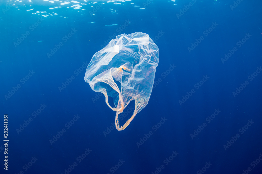 Underwater pollution:- A discarded plastic carrier bag drifting in a tropical, blue water ocean - obrazy, fototapety, plakaty 