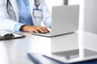 © rogerphoto - Unknown doctor woman typing on laptop computer while sitting at the desk in hospital office. close-up of hands. Physician at work. Medicine and health care concept