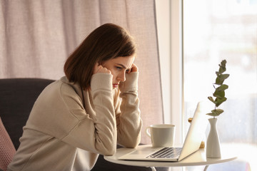 Depressed young woman using laptop at home