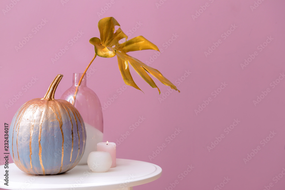 Painted pumpkin with burning candles on white table