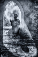 Wall Mural - black and white image of silhouette of muslim male praying in old mosque with lighting and smoke background