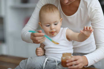 mother feeds baby with spoon in real kitchen