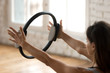 © fizkes - Young sporty attractive woman doing pilates toning exercise for arms and shoulders with ring, fitness with pilates magic circle in hands, working out, indoor close up. Strength, well being concept