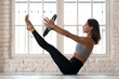 © fizkes - Young sporty attractive woman doing toning pilates exercise for abs, balance Paripurna Navasana pose with pilates magic circle in hands, working out wearing sportswear, indoor full length, yoga studio