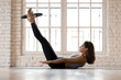 © fizkes - Young sporty attractive woman doing toning pilates the hundred exercise for abs with fitness circle, crunches for abdominal strength using pilates magic circle, practicing at yoga studio or at home