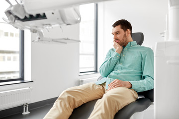 medicine, dentistry and healthcare concept - male patient suffering from toothache at dental clinic office