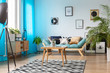 © Photographee.eu - Wooden coffee table with cactus in glass vase placed on patterned carpet in real photo of white and blue living room interior with fresh plants and posters on the wall