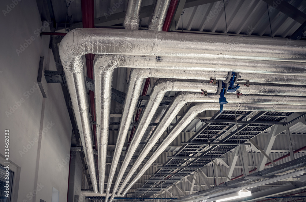 Metal pipes in thermal insulation winding on the ceiling of an industrial enterprise. - obrazy, fototapety, plakaty 