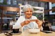 © Syda Productions - technology, old age and people concept - happy senior woman photographing dessert by smartphone at street cafe