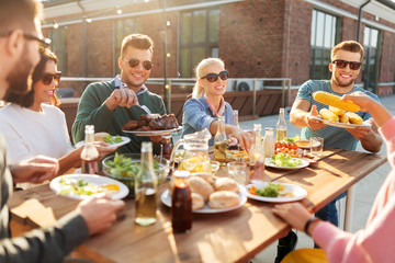 Canvas Print - leisure and people concept - happy friends eating and drinking at barbecue party on rooftop in summer