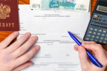 The man fills in the tax return, calculates the amount of tax on the calculator, The text in Russian: tax return.