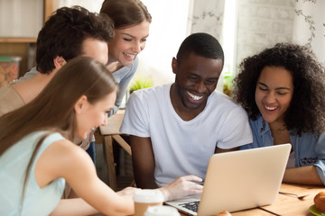 Black african guy with diverse friends watching comedy movie funny videos online using computer sitting together at desk. Friendship between multiracial people and leisure free time activities concept