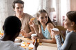© fizkes - Diverse young cheerful millennial people having dinner sitting at table in pizzeria eating pizza feels happy. Best friends gathered together spending weekend together talking chatting communicating