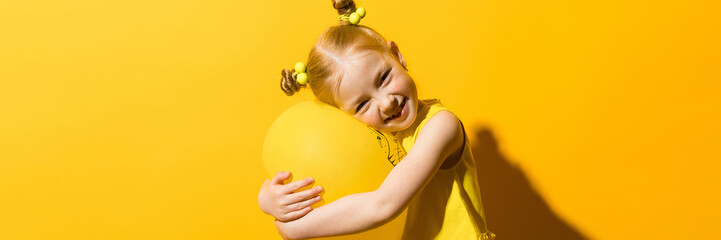 Wall Mural - Girl with red hair on a yellow background. A girl is hugging a yellow balloon.