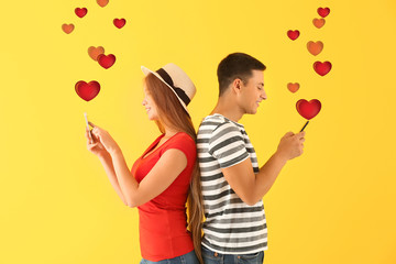 Young couple with mobile phones on yellow background. Online dating