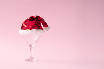 Poster - Martini or champagne glass with santas hat on pink background with copy space. Minimal flat lay Christmas theme. New year party concept.