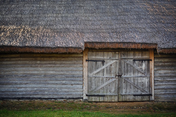 Old wooden barn. Log wall, gate and thatched roof.