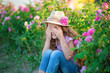 Cute brunette child blue eyes girl playing hide and seek joking in pink rose field. Wearing stylish dress and retro sunbonnet hat, enjoy summer time days childhood