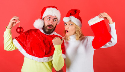 Wall Mural - Christmas stocking tradition. Christmas celebration concept. Woman and bearded man in santa hat waiting christmas red background. Couple christmas santa costume hold sock and ornament ball