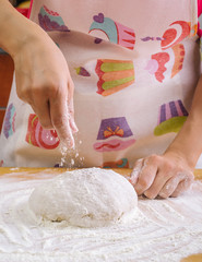 Woman sprinkles flour on a kneaded dough