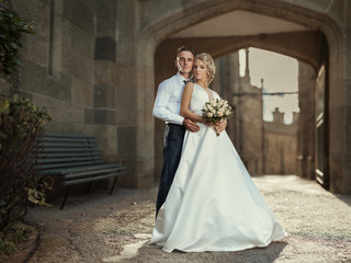 Wedding couple posing in the ancient city. Young cute bride with a bouquet of flowers and the groom embrace.