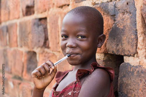Cuadros en Lienzo An 11-year old Ugandan girl smiling, holding a pen against her mouth and leaning