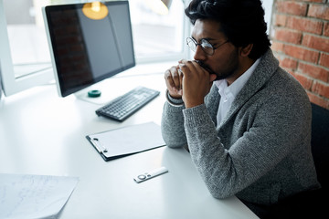 Indian guy with puzzled face sitting at the table. sadness, tiredness concept. close up side view shot