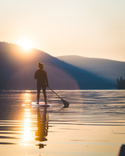 Young Woman On A Paddle Board In The Middle Of A Lake At Sunrise