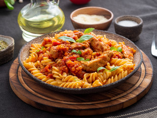 Wall Mural - fusilli pasta with tomato sauce, chicken fillet with basil leaves on dark brown background, side view