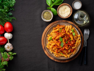 Wall Mural - fusilli pasta with tomato sauce, chicken fillet with basil leaves on dark brown background, top view, copy space