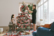 © Stocksy - A cute  girl and her mother decorating christmas tree at home
