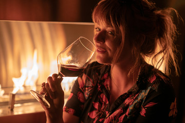 Wall Mural - Beautiful ginger girl drinking a glass of red wine near a fire pit