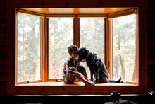 little boy sitting in a bay window with his black dog