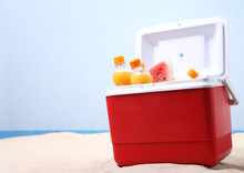 Open Ice Box With Orange Juice Bottles On White Sand At The Beach